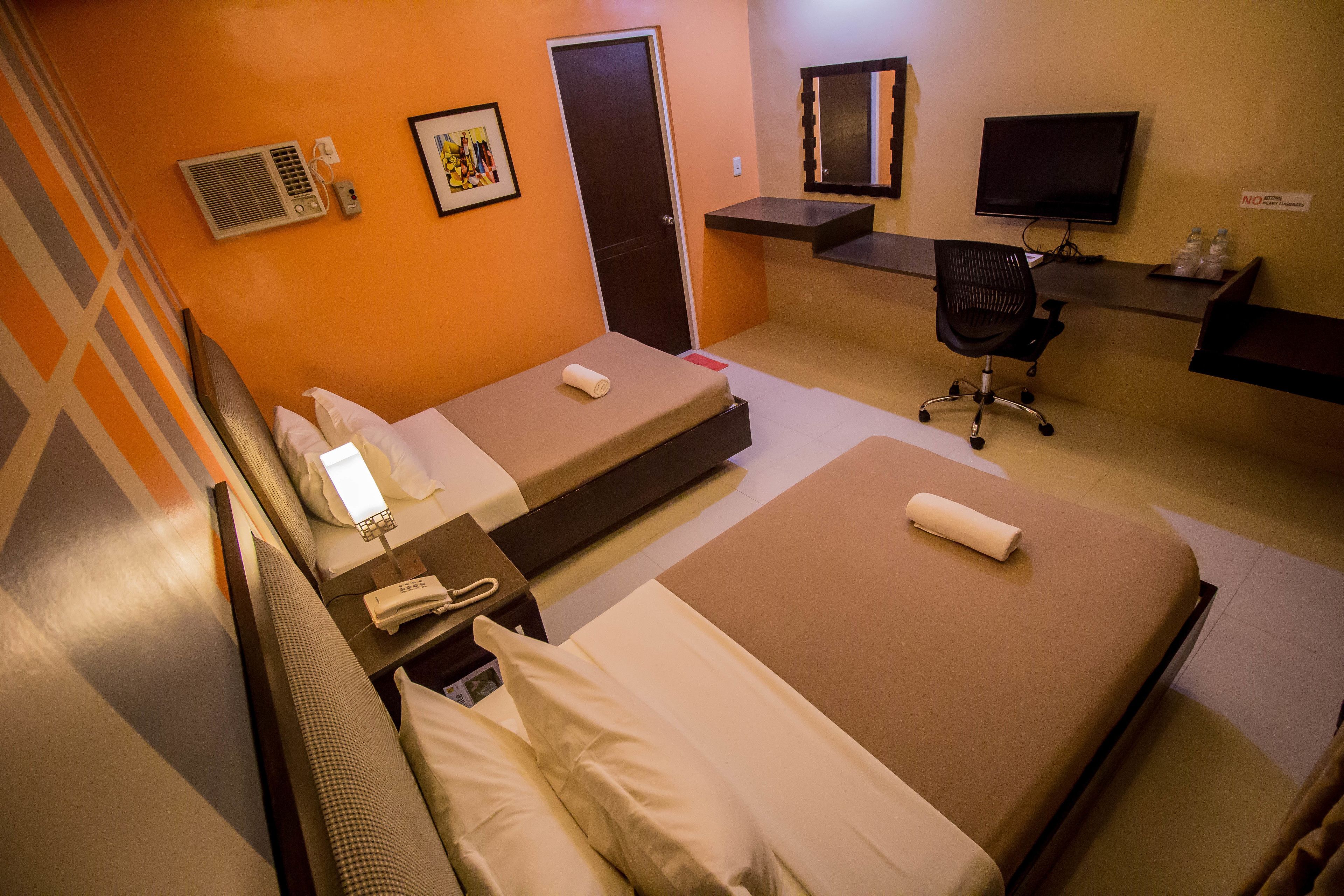 A hotel room with two beds, a desk with a chair, a television, and a bathroom.