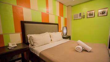 Habitación de hotel con cama, mesita de noche con teléfono, lámpara y pared con diseño a rayas.