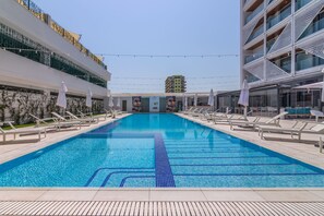 A swimming pool with lounge chairs and umbrellas, surrounded by modern buildings. - Nyota Hotel & Conference Center (Constanta)