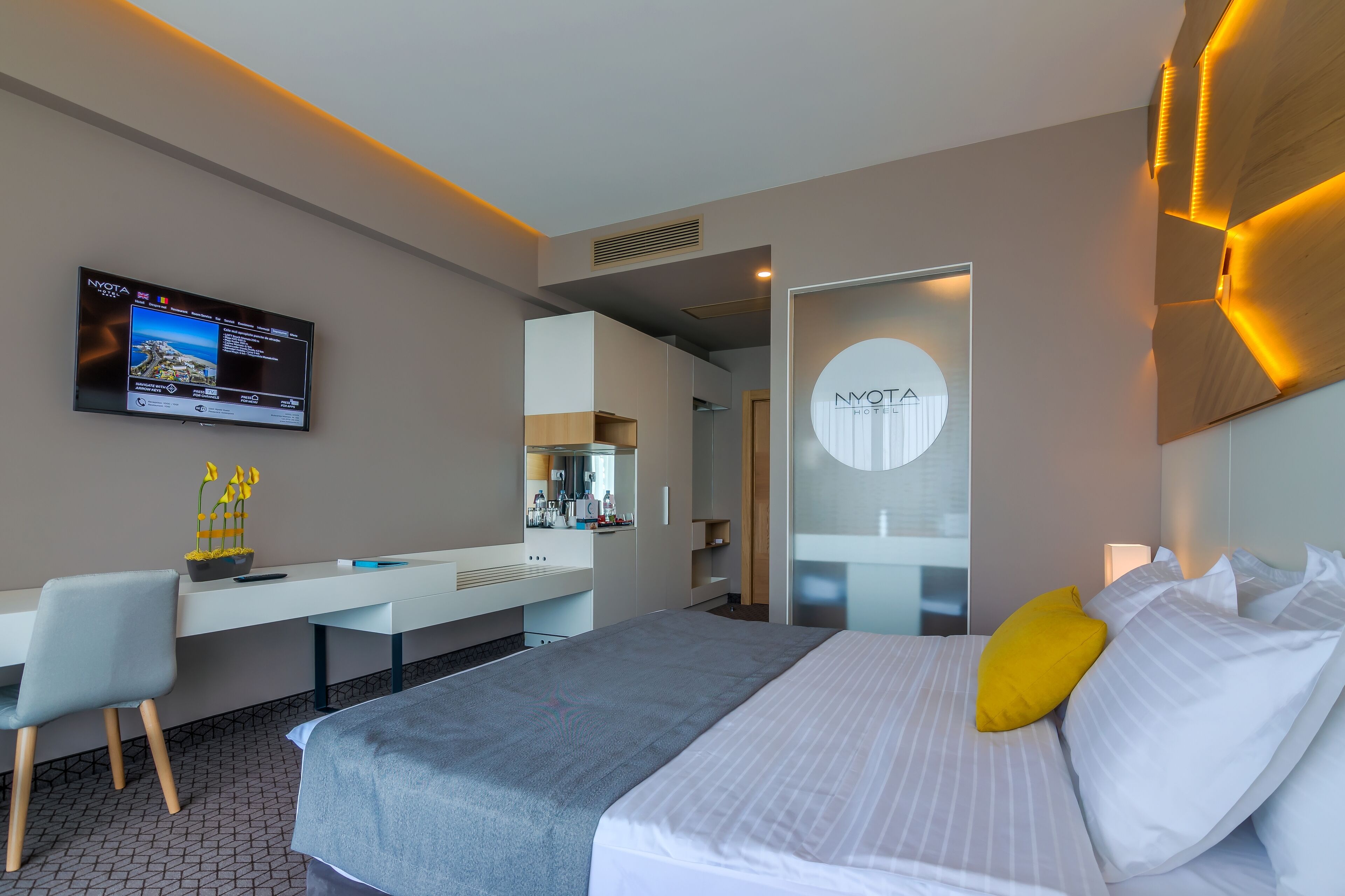 A modern hotel room with a bed, a desk, a chair, a TV, and a bathroom visible through an open door.