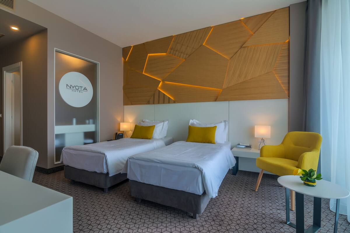A hotel room with two beds, a small table, a chair, and a decorative wall panel.