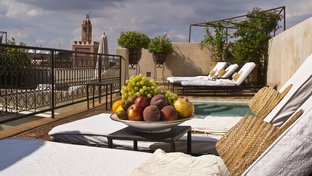 Un área junto a la piscina con sillones de descanso, un cuenco de frutas y vistas a un edificio con una torre.