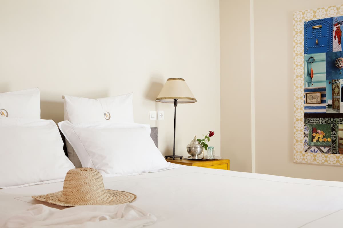 A neatly made bed with white linens, a bedside lamp, and a decorative mirror on the wall.