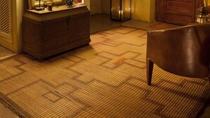 Un vestíbulo de hotel con un espejo grande, una lámpara, una planta en maceta, una puerta de madera y un sillón de cuero.