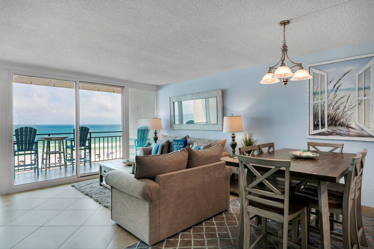 A living room with a sofa, dining table, chairs, and a view of the ocean through large sliding doors.