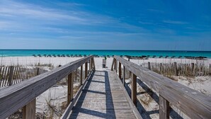 Une promenade en bois menant à une plage agrémentée de parasols et de chaises longues.