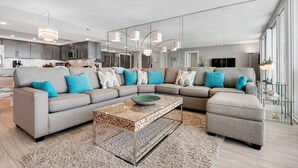 Un salon moderne avec un canapé d’angle, un pouf et une table basse en verre.