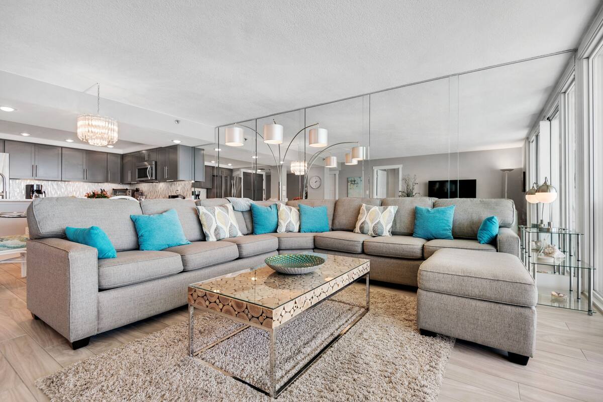 A modern living room with a sectional sofa, ottoman, and a glass coffee table.