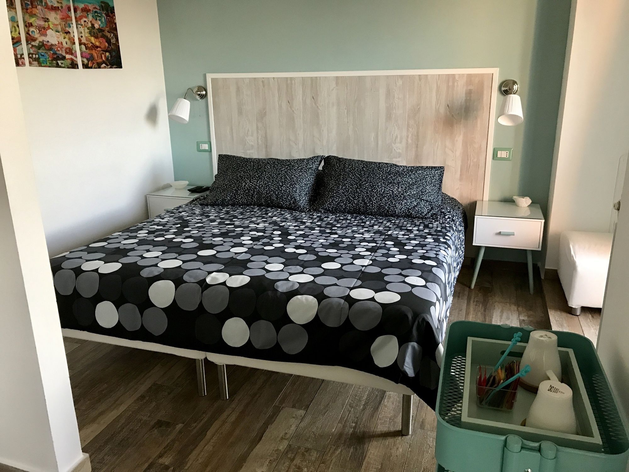 Ein Bett mit einem Punkte-Bettbezug, zwei Nachttische, ein Beistelltisch, eine grüne Mülleimer und eine Wandlampe.