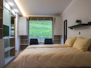 Quarto com uma cama grande, estantes embutidas, escrivaninha e janela com vista para uma área gramada.