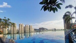 Una piscina con un diseño geométrico de azulejos, rodeada de edificios altos y palmeras.