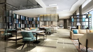 Un moderno vestíbulo de hotel con un amplio espacio de estar, una cocina al fondo y grandes ventanales que aportan luz natural.