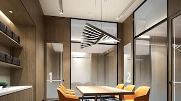 A modern conference room with a wooden table, four orange chairs, and a unique ceiling light fixture.