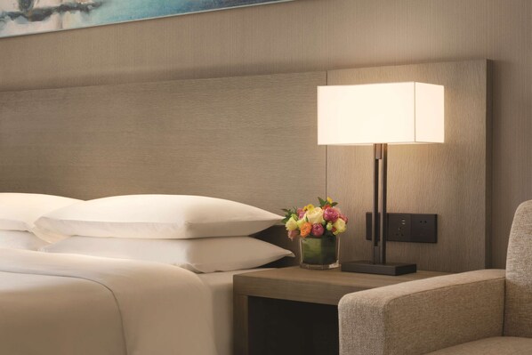 Une chambre d’hôtel avec un lit bien fait, une table de chevet avec une lampe et un vase de fleurs, et une chaise.