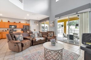 Relax in this inviting living space with a comfortable sofa, coffee table, and potted plant, leading to a patio with dining area.
