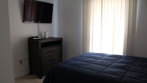 A bedroom with a bed, a dresser, a television mounted on the wall, and a window with curtains.