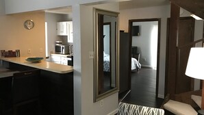 Kompakti hotellihuone, jossa on pieni keittiönurkkaus, kuviollinen päiväpeiteellä varustettu sänky, peili ja pieni oleskelualue, jossa on tuoli ja pöytä.
