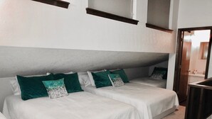 Hotellihuoneessa on kaksi sänkyä, joissa on valkoiset lakanat ja vihreät tyynyt. Huoneen sisustus on pelkistetty ja moderni, ja siinä on harmaa seinä sekä puinen sängynpääty.