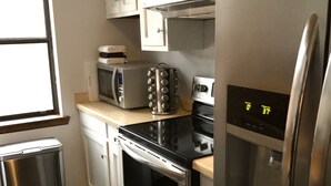 Moderni keittiö, jossa on ruostumattomasta teräksestä valmistetut kodinkoneet, kuten jääkaappi, uuni ja mikroaaltouuni. Keittiössä on ikkuna, josta tulee luonnonvaloa, sekä roskakori.