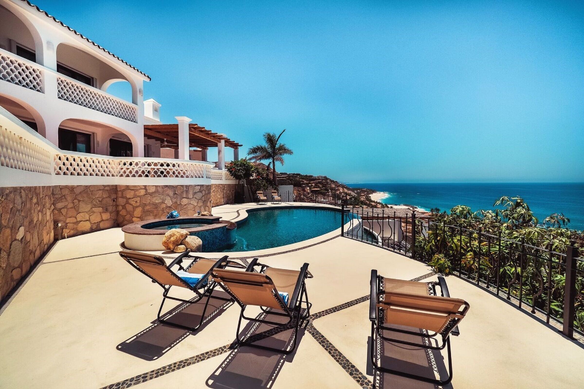 A pool area with lounge chairs and a hot tub, overlooking a coastal view.