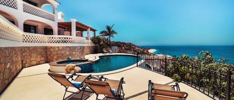 A pool area with lounge chairs and a hot tub, overlooking a coastal view.