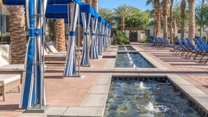 Un espace piscine aménagé avec des chaises longues, une fontaine et des palmiers.