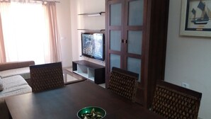 Sala de estar com televisão, sofá e mesa de jantar.