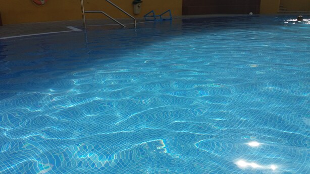 Piscina interior translúcida, com reflexos visíveis na água e uma escada.