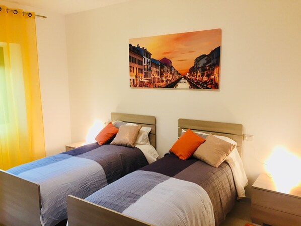 A hotel room with two beds, each with a headboard, and a painting of a cityscape on the wall.