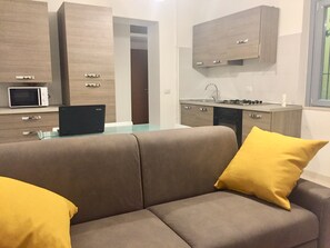 Una cocina moderna con microondas, estufa y armarios. Se aprecia un sofá con cojines amarillos al frente.