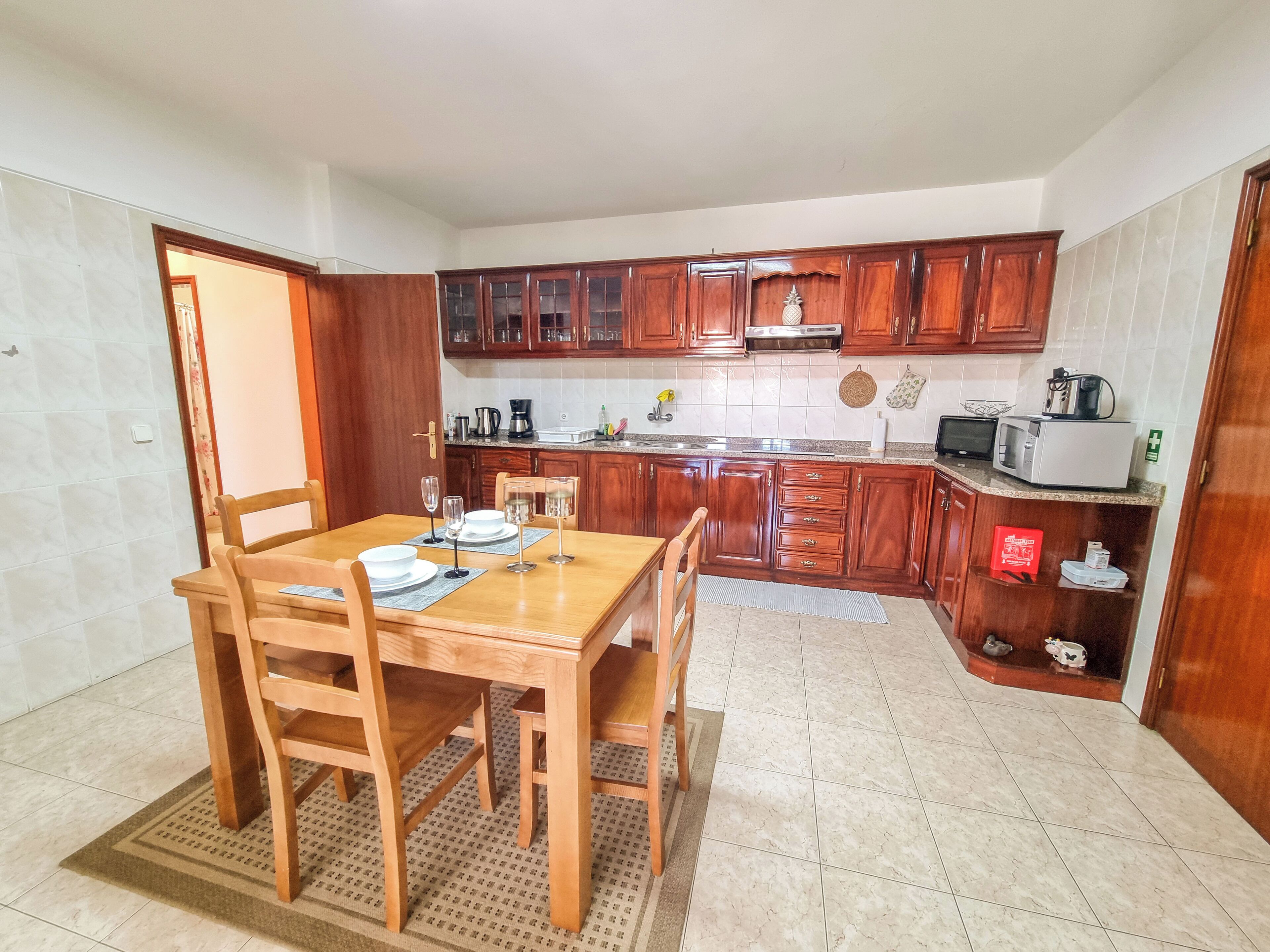 Una cocina compacta con armarios de madera, una mesa de comedor preparada para cuatro personas y un microondas en la encimera.