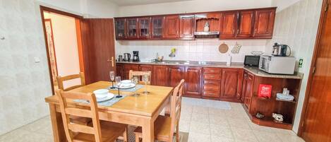 Una cocina compacta con armarios de madera, una mesa de comedor preparada para cuatro personas y un microondas en la encimera.