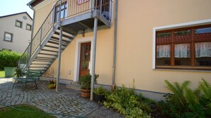 En tvåvåningsbyggnad med en metalltrappa, en trädörr och ett fönster med en gardin.