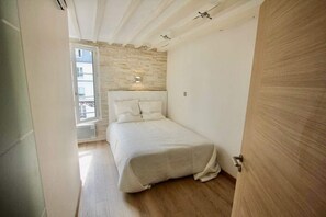 A bedroom with a stone wall, a bed with white bedding, and a wooden door.
