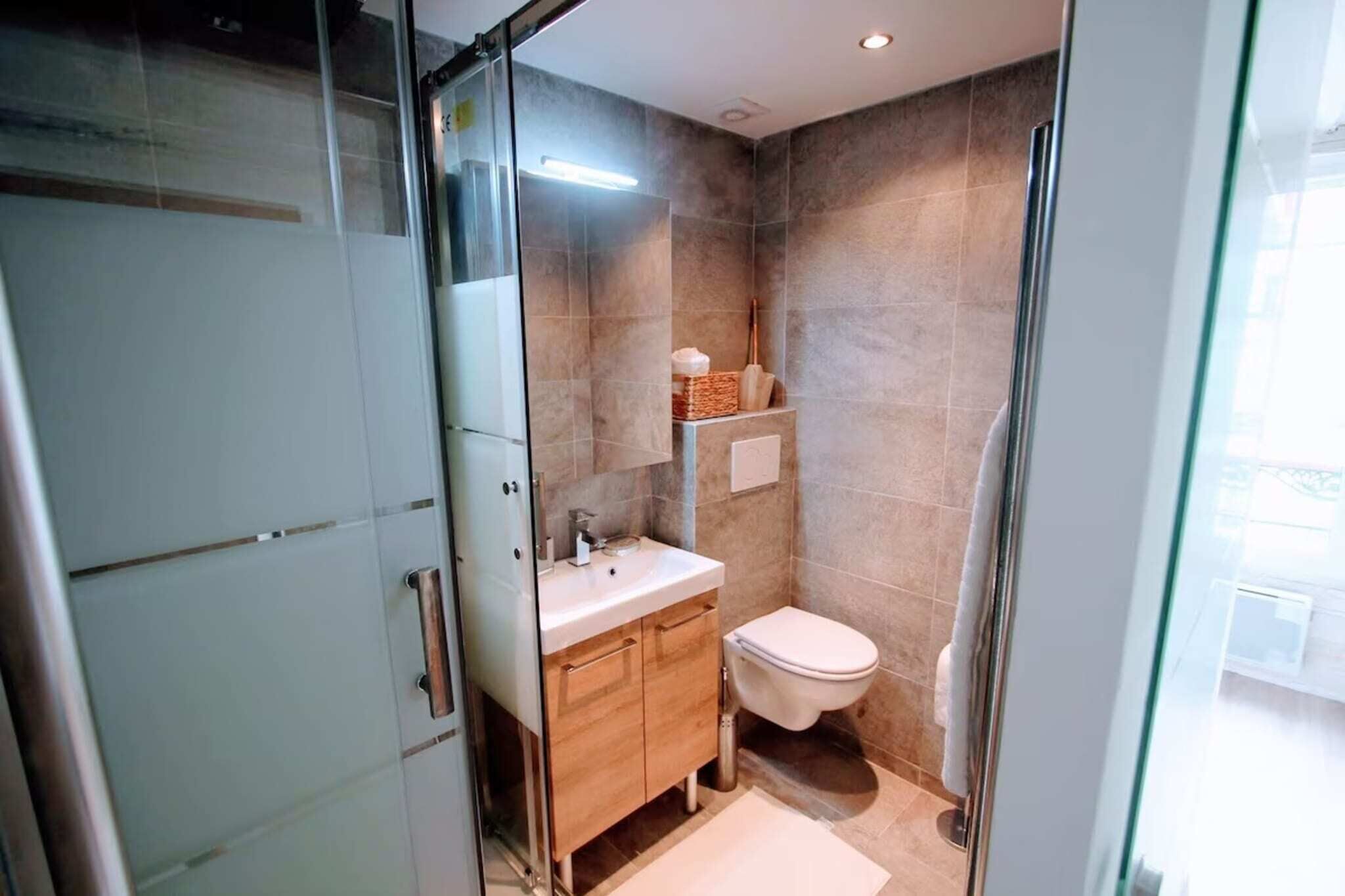 A modern bathroom with a glass shower enclosure, a wooden vanity, and a toilet.