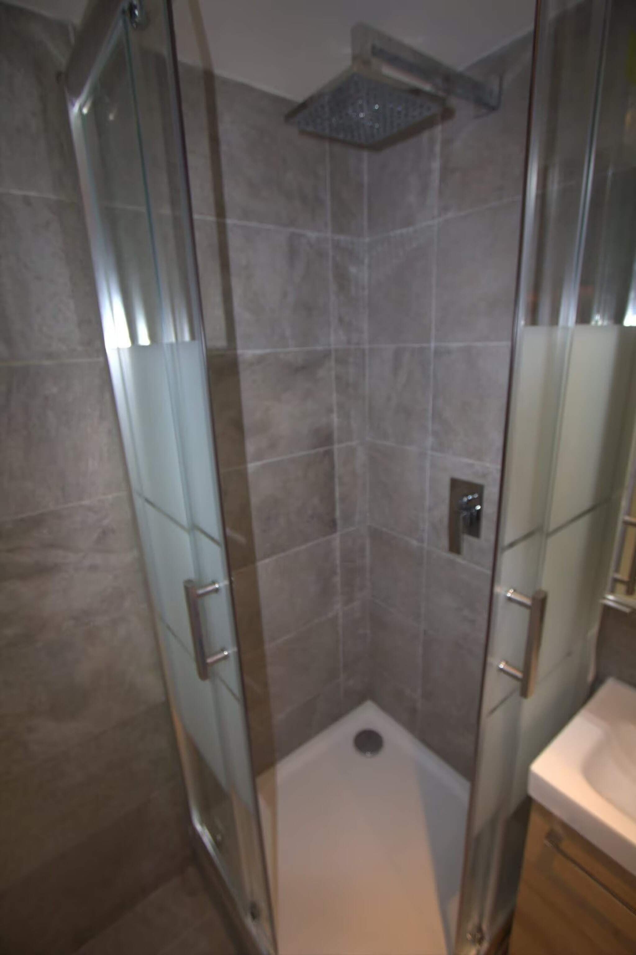 Eine begehbare, gläserne Dusche mit Duschkopf, eine weiße Badewanne und ein modernes Badezimmerdesign.