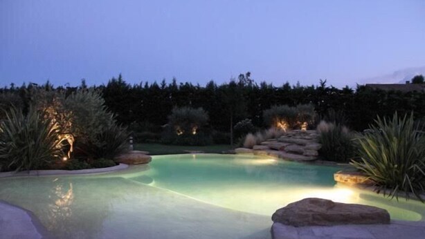 A swimming pool with a clear water surface, surrounded by rocks and plants, and illuminated by soft lighting. - Provencal country house with heated freeform pool (Châteaurenard)