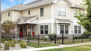 A two-story residential building with a front porch, a black metal fence, and a small garden area. - Top-Floor 1-Bedroom Condo in Downtown Traverse City – Walk to Beaches & Dining (Traverse City)
