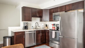 A modern kitchen with dark wooden cabinets, stainless steel appliances, and a white countertop. - Top-Floor 1-Bedroom Condo in Downtown Traverse City – Walk to Beaches & Dining (Traverse City)