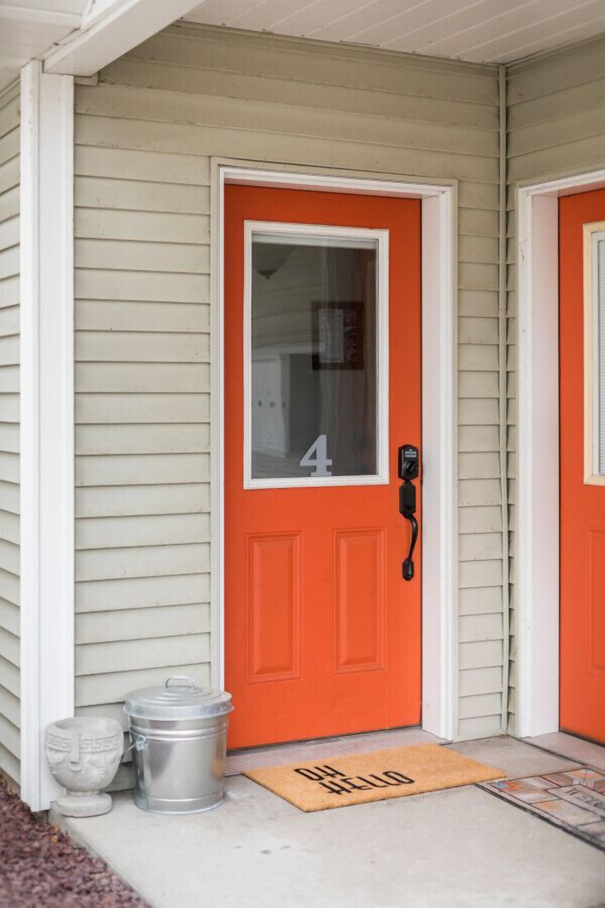 A house with a bright orange door, a mailbox, and a doormat.