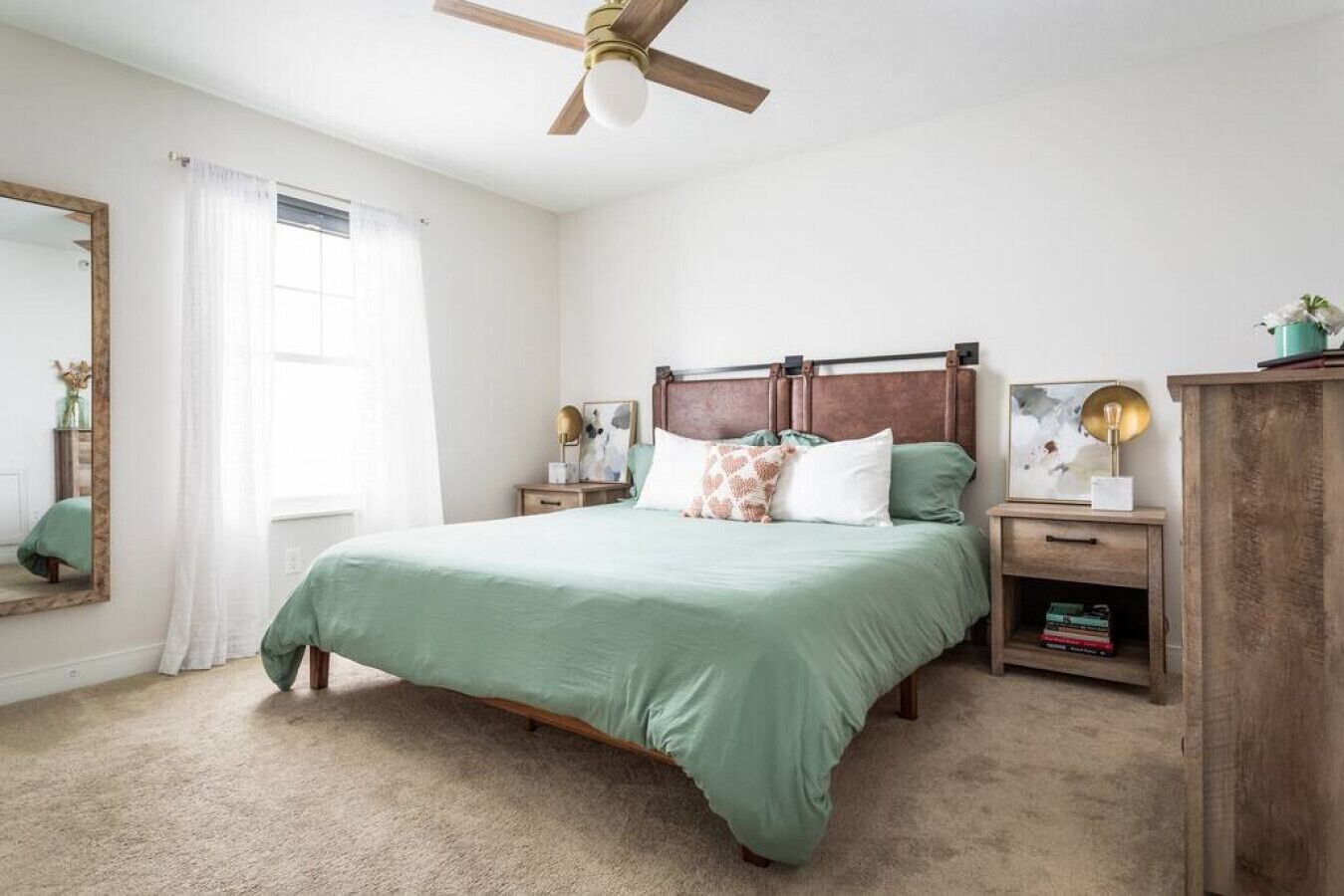 A bedroom with a bed, nightstands, a wardrobe, a ceiling fan, and a window with curtains.