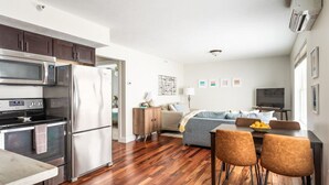 A modern kitchen with stainless steel appliances, a dining area with wooden chairs, and a living space with a sofa and TV. - Top-Floor 1-Bedroom Condo in Downtown Traverse City – Walk to Beaches & Dining (Traverse City)