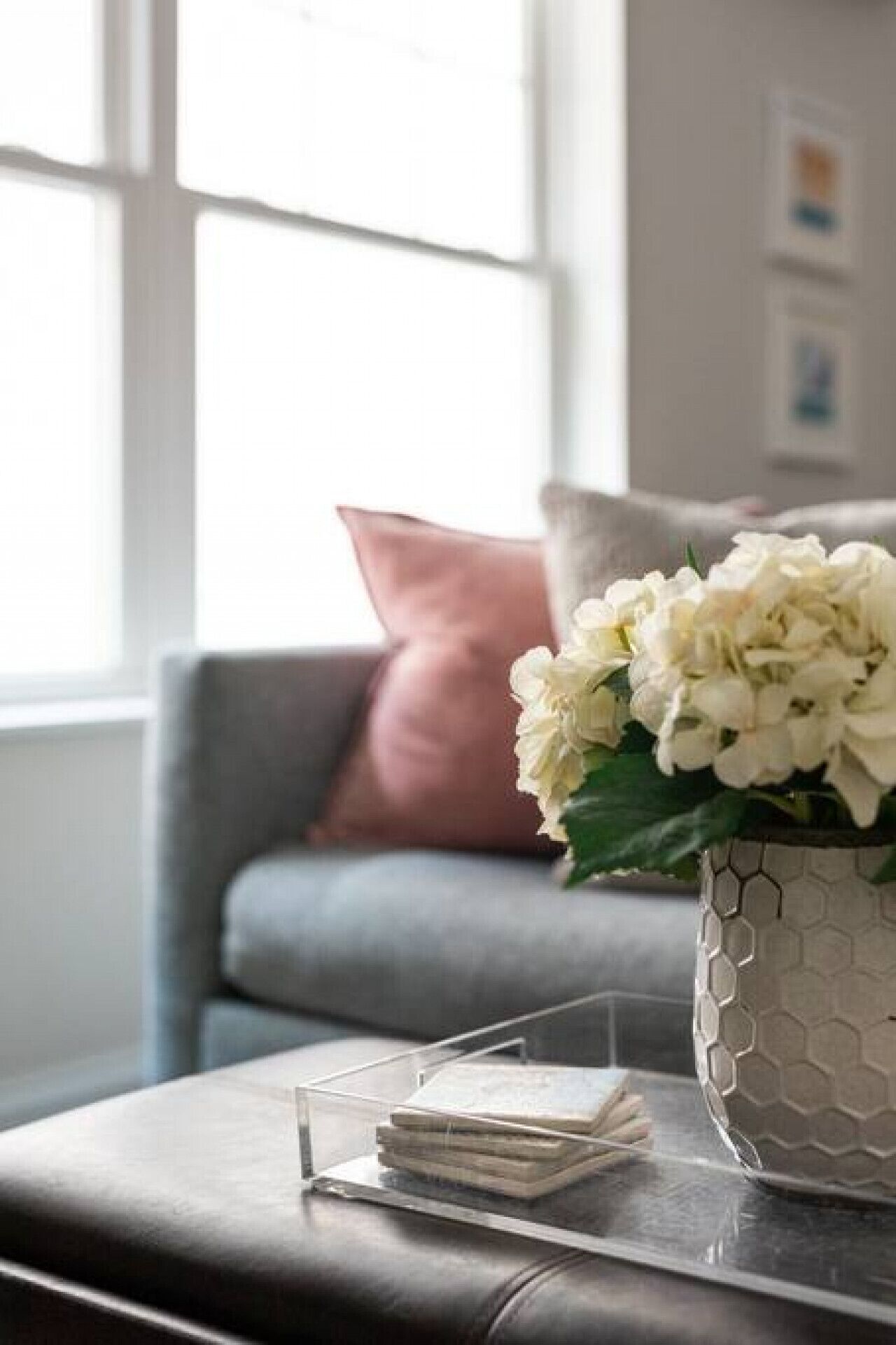 Un salon moderne avec un canapé gris, un vase blanc orné de fleurs et une petite table d’appoint en acrylique transparent sur laquelle sont posés des livres.