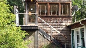 Ein zweistöckiges Holzhaus mit Balkon, Satellitenschüssel und einem Garten mit Mulch und Pflanzen.