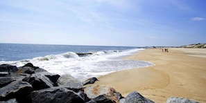 Uma praia com ondas, rochas e algumas pessoas ao longe.