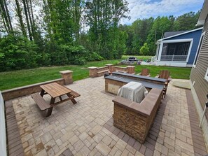 Eine Terrasse mit einem Holztisch, einem Grill und Steinsitzgelegenheiten.