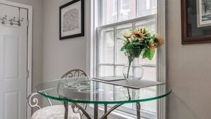 A glass-top table with a metal frame, a white cushioned chair, and a vase with sunflowers on a windowsill. - RETREAT on the CREEK - Businees Travelor or Weekend Getaway. HISTORIC DISTRICT. (Frederick)