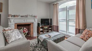 A living room with a fireplace, a television, and a large window with curtains. - RETREAT on the CREEK - Businees Travelor or Weekend Getaway. HISTORIC DISTRICT. (Frederick)