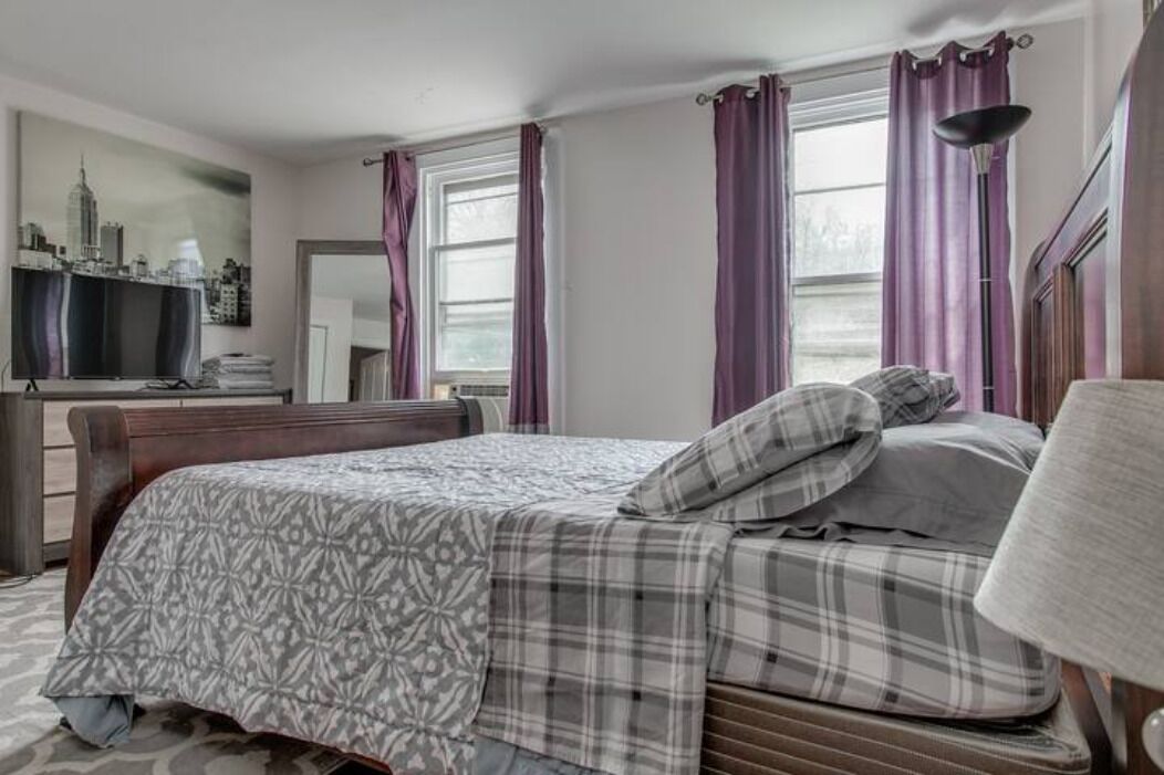 A bedroom with a bed, a desk, a chair, and a window with curtains.