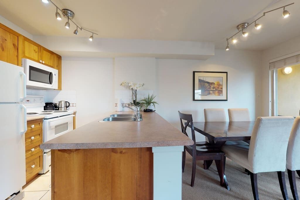 A modern kitchen with a central island, wooden cabinets, and a dining area with a table and chairs.